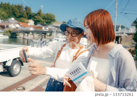 60代シニアと20代女性が旅先でスマホを見るシーン 60代シニアと20代女性が旅先でスマホを見るシーン 133713261