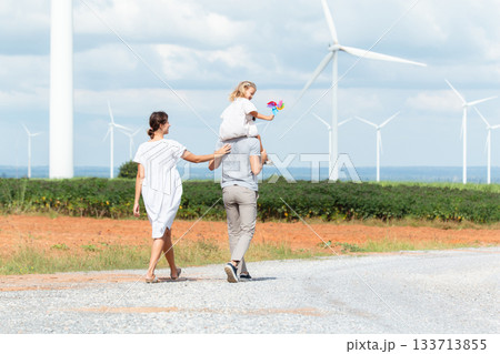 Happy cheerful caucasian white family with daughter are walking and relaxing together in the daytime in nature with windmill towers in background. Happy family activity concept. Happy cheerful caucasian white family with daughter are walking and relaxing together in the daytime in nature with windmill towers in background. Happy family activity concept. 133713855