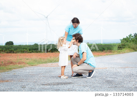 Happy cheerful caucasian white family with daughter are walking and relaxing together in the daytime in nature with windmill towers in background. Happy family activity concept. Happy cheerful caucasian white family with daughter are walking and relaxing together in the daytime in nature with windmill towers in background. Happy family activity concept. 133714003