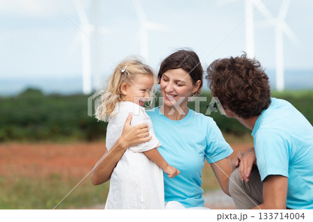 Happy cheerful caucasian white family with daughter are walking and relaxing together in the daytime in nature with windmill towers in background. Happy family activity concept. Happy cheerful caucasian white family with daughter are walking and relaxing together in the daytime in nature with windmill towers in background. Happy family activity concept. 133714004