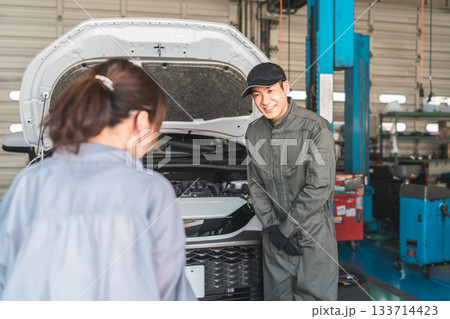 整備工場で車の説明をする整備士の男性スタッフとドライバーの女性客 133714423