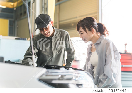 車のエンジンルームで女性客に説明,解説をする整備士,メカニックの男性スタッフ 車のエンジンルームで女性客に説明,解説をする整備士,メカニックの男性スタッフ 133714434