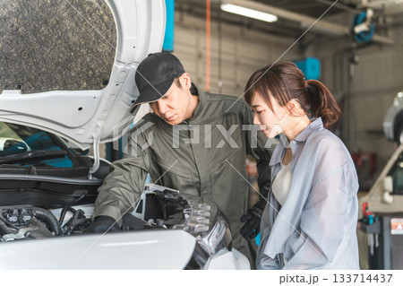 車のエンジンルームで女性客に説明,解説をする整備士,メカニックの男性スタッフ 車のエンジンルームで女性客に説明,解説をする整備士,メカニックの男性スタッフ 133714437