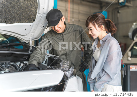 車のエンジンルームで女性客に説明,解説をする整備士,メカニックの男性スタッフ 133714439