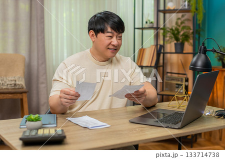 Asian man stacking paid bills, relieved smile shows satisfaction after clearing monthly statements Asian man stacking paid bills, relieved smile shows satisfaction after clearing monthly statements 133714738