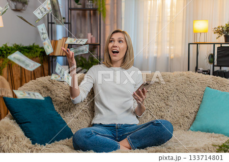 Woman celebrates lottery jackpot with dollar cash falling down while reads win message on smartphone Woman celebrates lottery jackpot with dollar cash falling down while reads win message on smartphone 133714801
