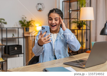 Excited happy joyful Caucasian young woman girl using smartphone sitting at home office table 133714932