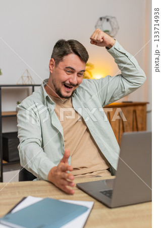 Happy young Caucasian man working on laptop shocked by sudden victory sitting at home office table 133714938