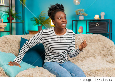 African American woman angry punching pillow sofa frustration emotional indoors intense reaction 133714943
