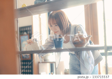 カフェ雑貨を手に取る20代女性のローカル散策シーン 133715537