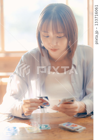 光の差すカフェでカードゲームを楽しむ20代女性 光の差すカフェでカードゲームを楽しむ20代女性 133716061