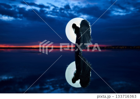 Young lady with wings in fight circle, night photography, dramatic sky, water reflection 133716363