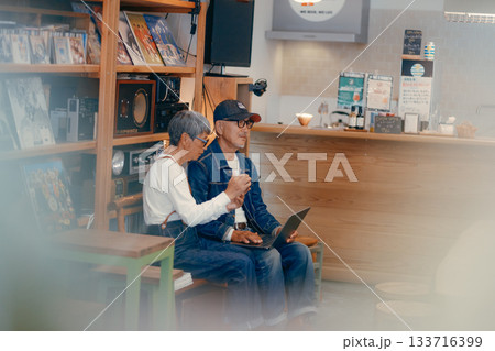 シニア夫婦がカフェでパソコンとスマホを使って調べものをするシーン シニア夫婦がカフェでパソコンとスマホを使って調べものをするシーン 133716399