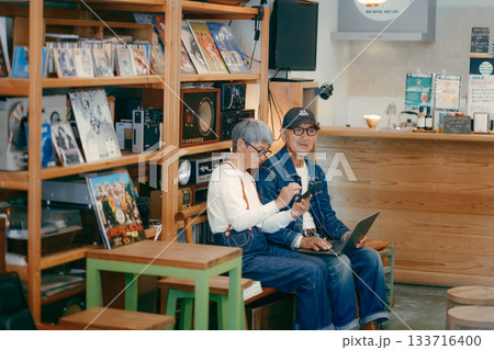 シニア夫婦がカフェでパソコンとスマホを使って調べものをするシーン 133716400