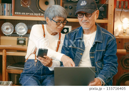 シニア夫婦がカフェでパソコンとスマホを使って調べものをするシーン 133716405