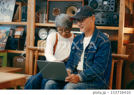 シニア夫婦がカフェでパソコンとスマホを使って調べものをするシーン 133716410