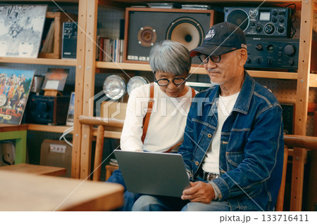 シニア夫婦がカフェでパソコンとスマホを使って調べものをするシーン 133716411
