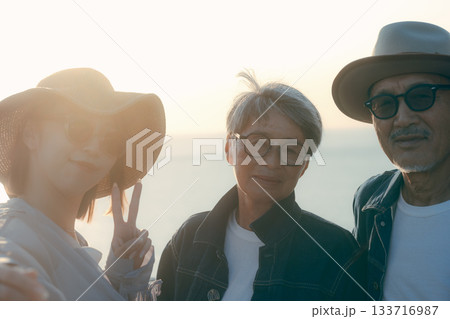 夕暮れの海辺で親子3人が自撮りを楽しむシーン 133716987