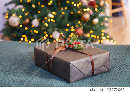 Christmas gift box decorated with ribbon and red berries in front of glowing festive tree lights 133720454