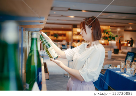 ホテルのお土産コーナーで地酒を選ぶ20代女性OL ホテルのお土産コーナーで地酒を選ぶ20代女性OL 133720885