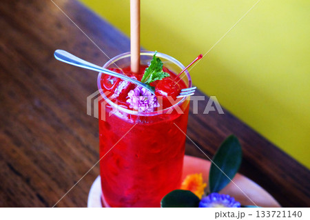 Close up a glass of red soda with a cherry and violet flower decorated on topping on wooden table Close up a glass of red soda with a cherry and violet flower decorated on topping on wooden table 133721140