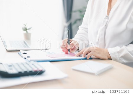 Concept of business planning and financial analysis. A businesswoman writes notes on documents with charts and reports, using laptop and calculator for budget management at modern office desk. Concept of business planning and financial analysis. A businesswoman writes notes on documents with charts and reports, using laptop and calculator for budget management at modern office desk. 133721165