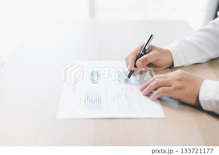 Businessman reviews financial reports, points on chart with pen while analyzing data at office desk working with calculator for accuracy. Concept of accounting, business planning, investment strategy. Businessman reviews financial reports, points on chart with pen while analyzing data at office desk working with calculator for accuracy. Concept of accounting, business planning, investment strategy. 133721177