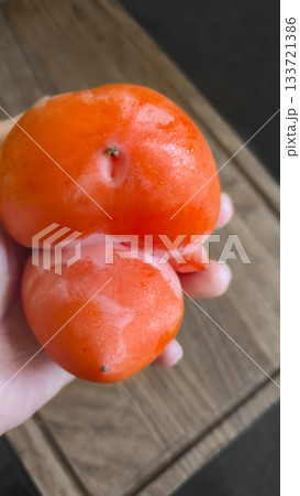 An ugly, natural persimmon on a wooden board, ripe and oddly shaped. ugly food. 133721386