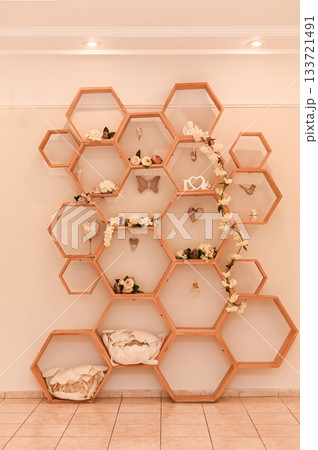 modern shelf with hexagonal compartments filled with decorative items such as small plants and soft fabrics. elegant hexagonal shelf arrangement featuring decorative pieces. modern shelf with hexagonal compartments filled with decorative items such as small plants and soft fabrics. elegant hexagonal shelf arrangement featuring decorative pieces. 133721491