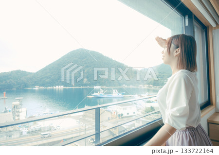 20代 女性がホテルの窓辺で景色を眺めるシーン 133722164