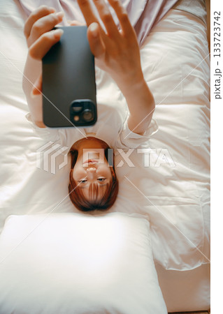 20代 女性がホテルのベッドでスマホを持ち自撮りするシーン 133723742