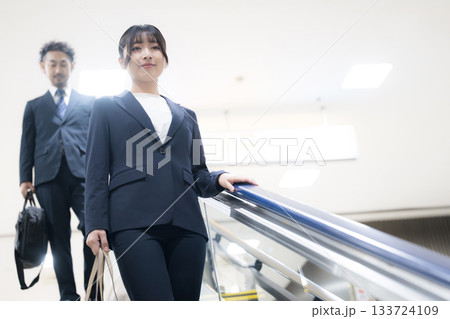 空港や駅のエスカレーターを降りるスーツ姿のキャリア女性のビジネス移動シーン 133724109
