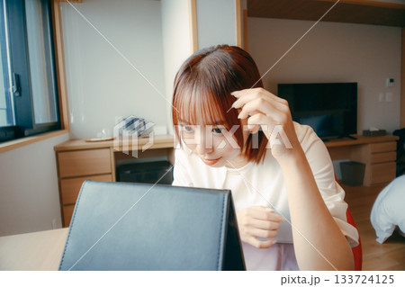 20代 女性がホテルの部屋で鏡を見て身だしなみを整えるシーン｜旅行・宿泊・メイク 133724125