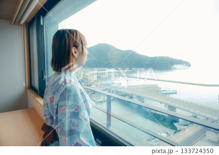 浴衣姿の20代女性がホテルの窓辺から海を眺めるシーン 133724350