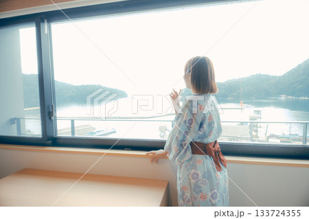 浴衣姿の20代女性がホテルの窓辺から海を眺めるシーン 133724355