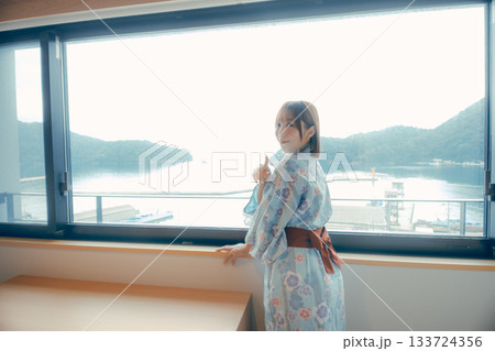 浴衣姿の20代女性がホテルの窓辺から海を眺めるシーン 133724356