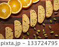 Row of home baked biscotti cookies, arranged diagonally with pistachio nuts and orange slices 133724795