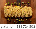 Pistachio biscotti cookies surrounded by pistachios on a wood cutting board 133724802