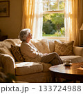窓の外を部屋のソファから見ている白髪のシニア女性 133724988