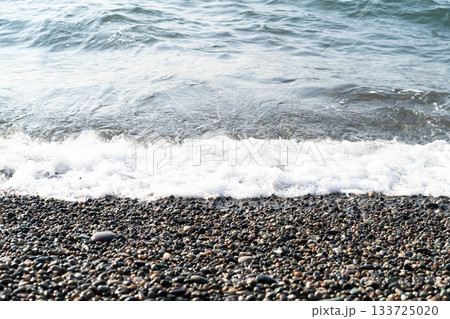 Waves gently lap against a beautiful pebble beach, creating a serene atmosphere perfect for relaxation. The vibrant blue sea and clear sky enhance the luxurious feel of a spa getaway. Waves gently lap against a beautiful pebble beach, creating a serene atmosphere perfect for relaxation. The vibrant blue sea and clear sky enhance the luxurious feel of a spa getaway. 133725020