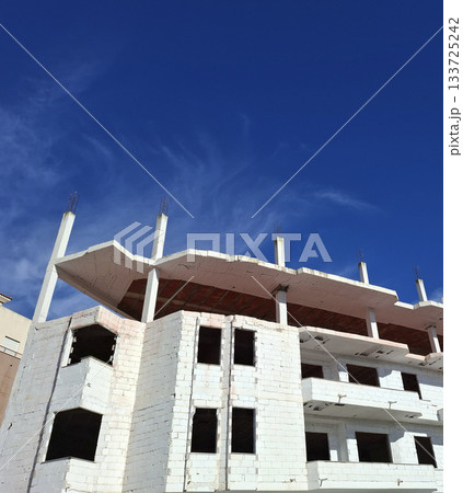 A white brick house stands tall under construction, with its framework visible against a bright blue sky. The scene captures the progress of modern housing development. A white brick house stands tall under construction, with its framework visible against a bright blue sky. The scene captures the progress of modern housing development. 133725242