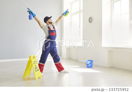 Happy smiling man cleaner in uniform having fun in empty apartments holding detergent in hands Happy smiling man cleaner in uniform having fun in empty apartments holding detergent in hands 133725952