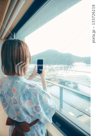 浴衣姿の20代女性がホテルの窓から景色を眺めるシーン 133726219