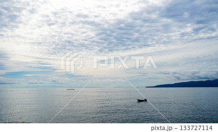 雲がかった空の下に広がる海原と釣り船のシルエット 133727114