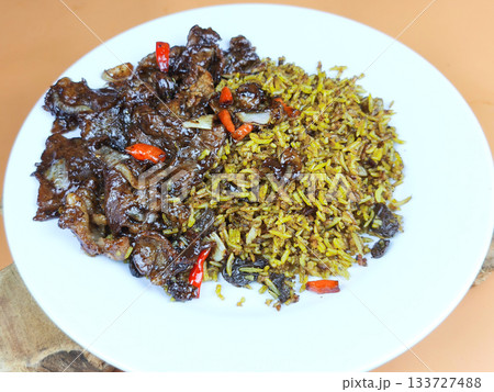 Indonesian Nasi Kebuli with flavorful spiced rice and rich, dark beef or mutton pieces, garnished with chilies, served on a white plate. Traditional Middle Eastern influenced rice dish. Indonesian Nasi Kebuli with flavorful spiced rice and rich, dark beef or mutton pieces, garnished with chilies, served on a white plate. Traditional Middle Eastern influenced rice dish. 133727488