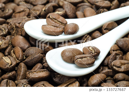 Beans of coffee in ceramic spoons on roasted coffee background Beans of coffee in ceramic spoons on roasted coffee background 133727687