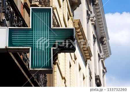 Green neon pharmacy cross with cracked glass symbolizing healthcare problems, medicine shortages, and systemic fragility 133732260