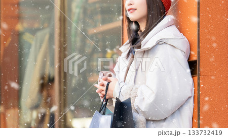 雪の降る冬の街角に立つ笑顔の女性 133732419