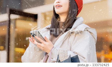 雪の降る冬の街角でスマートフォンを使う女性 雪の降る冬の街角でスマートフォンを使う女性 133732425