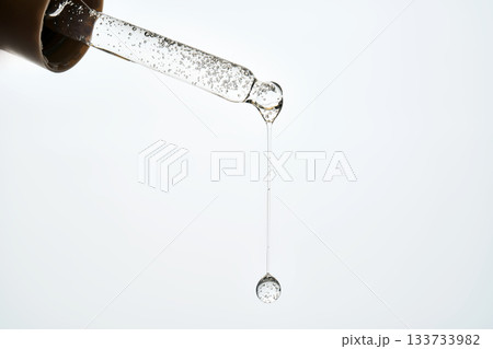 Cosmetic pipette dispensing serum drop against white background Cosmetic pipette dispensing serum drop against white background 133733982